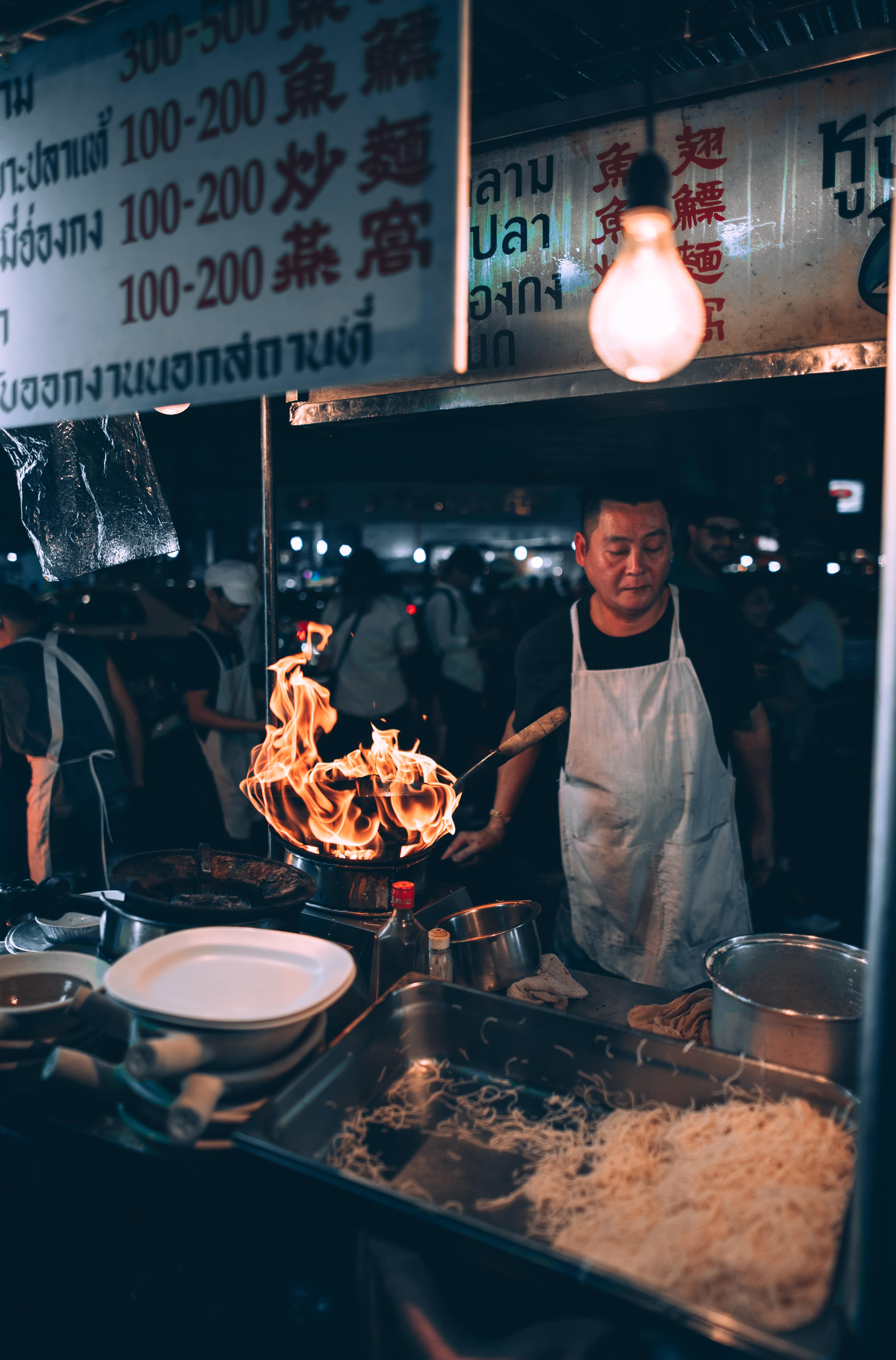 Fiery wok in front of man who is selling fried noodles