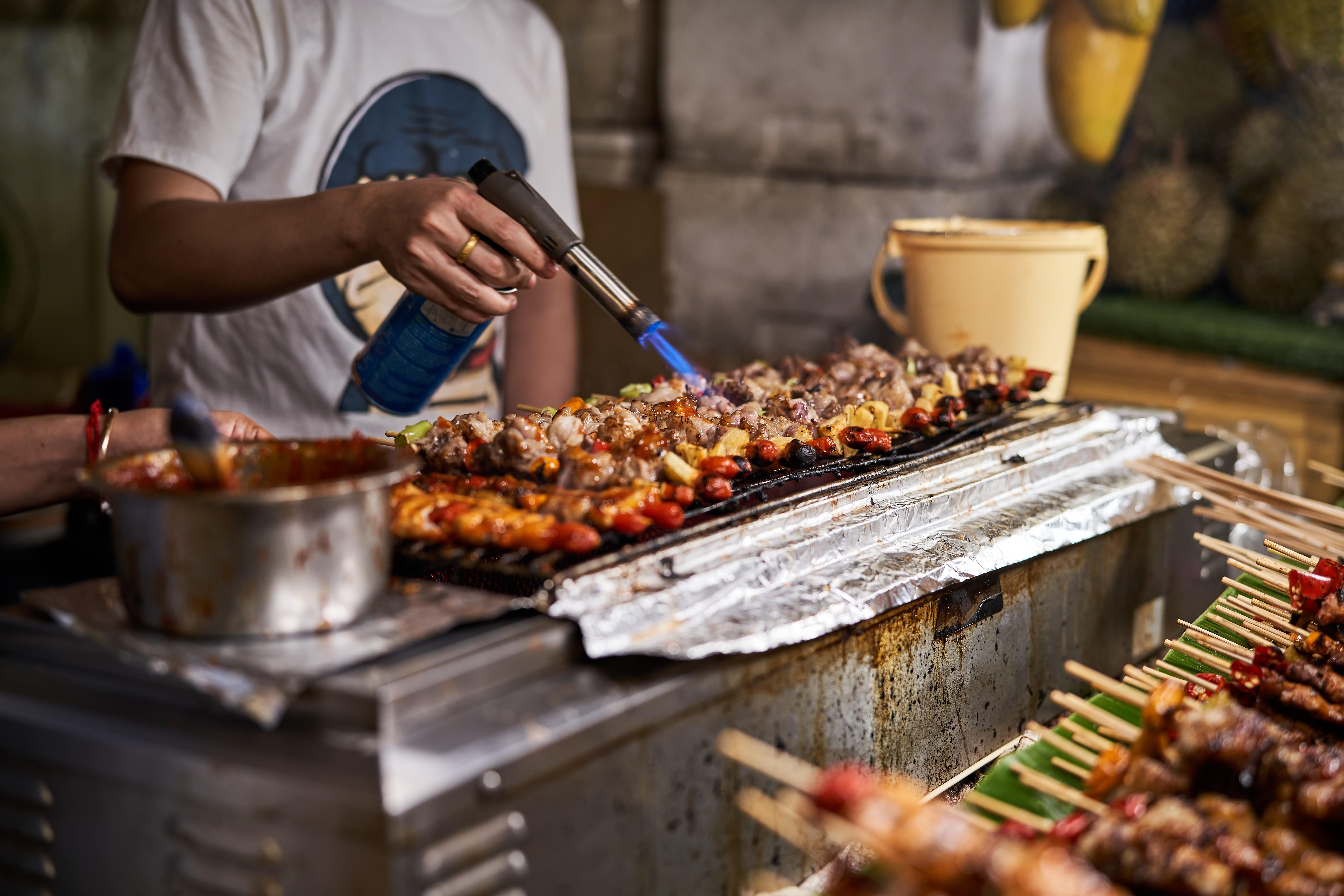 Person grilling many meat skewers