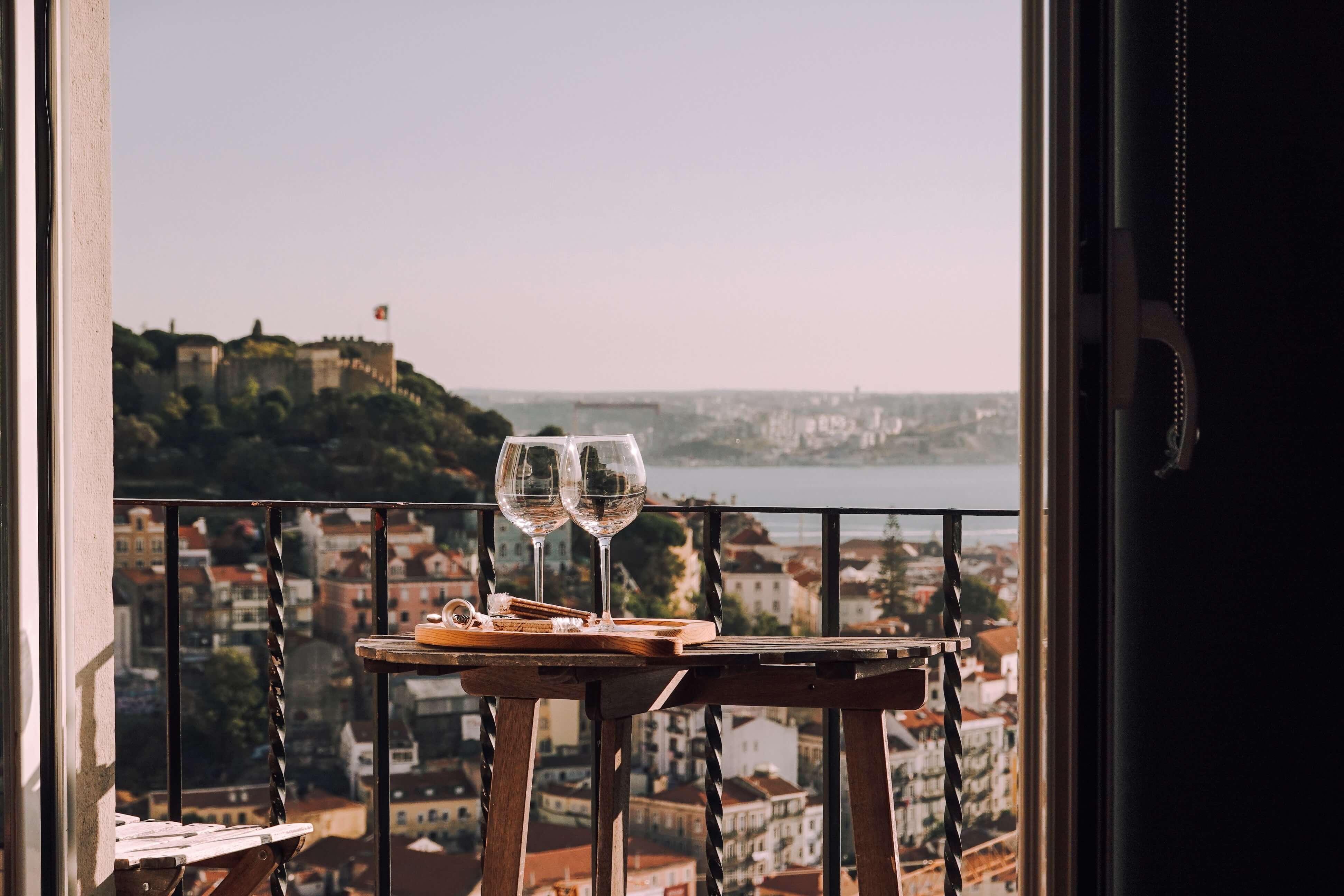 2 wine glasses perched on a table top, with a beautiful scenery of a city in the background