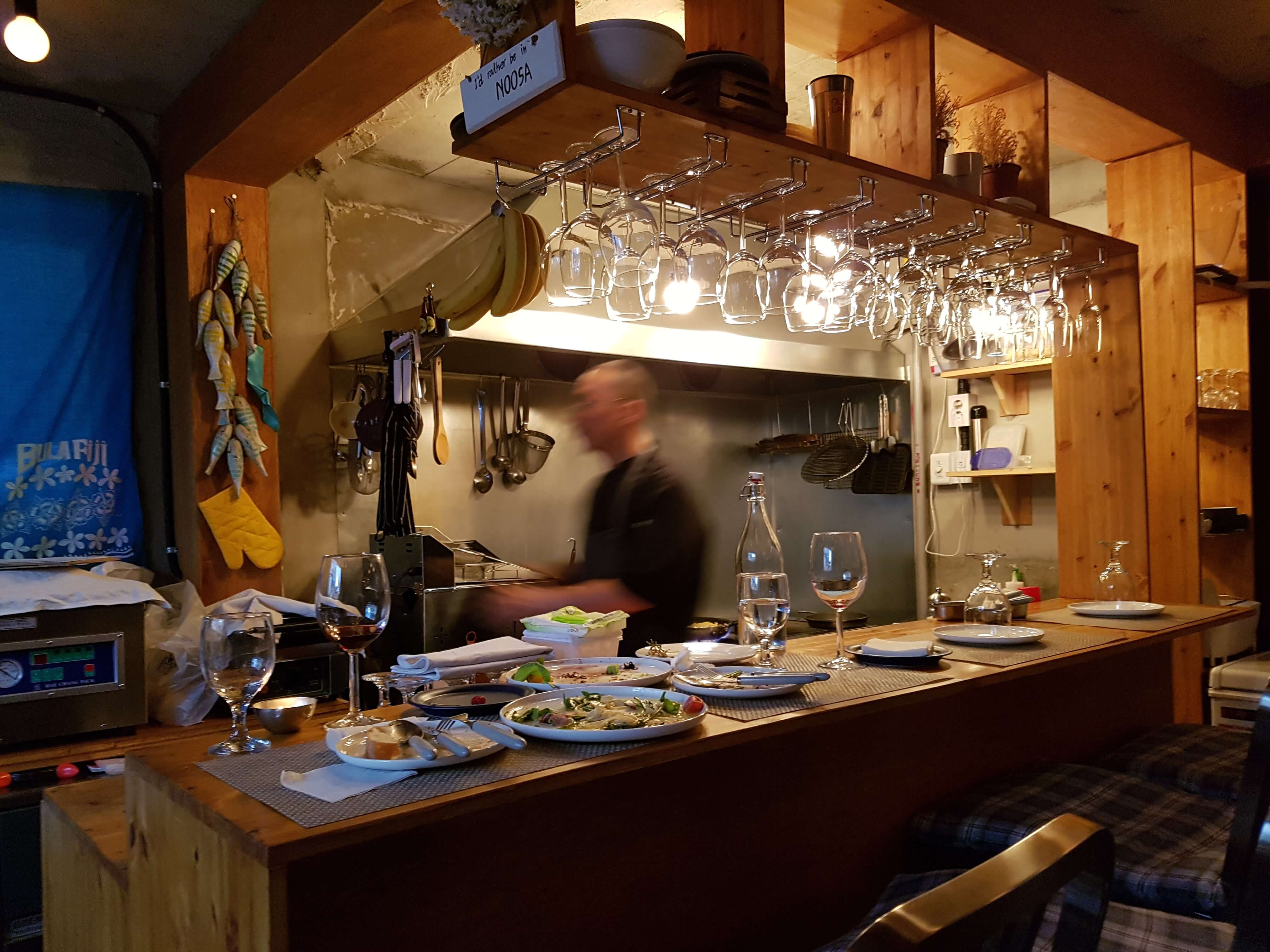 Cozy restaurant with lots of wine glasses, and a busy chef in the background