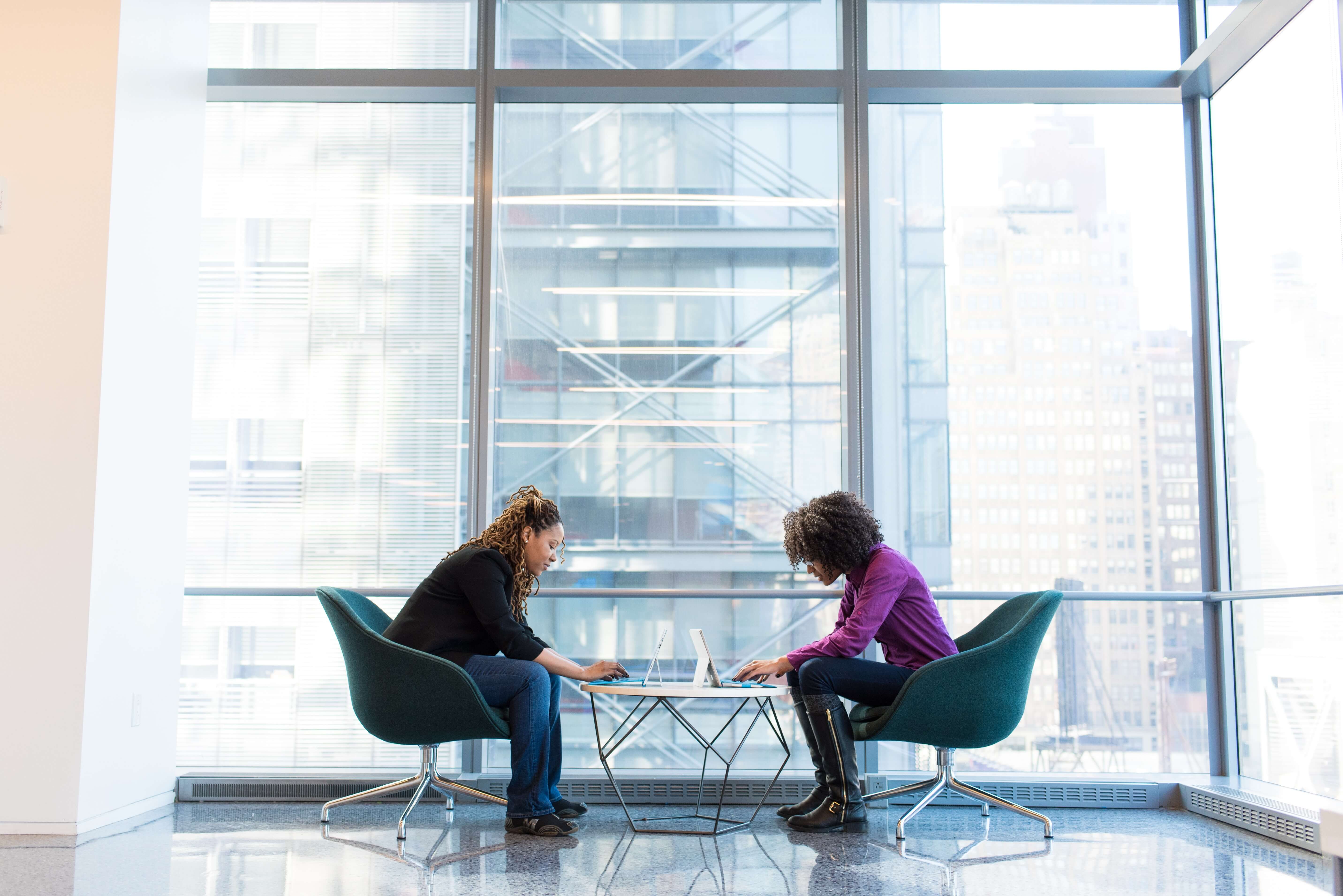 2 Women sitting down in a office, doing their work on their laptop